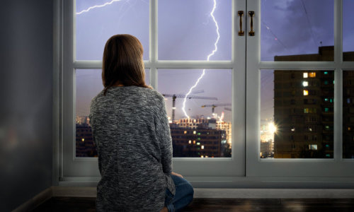 girl looks at lightning through window 