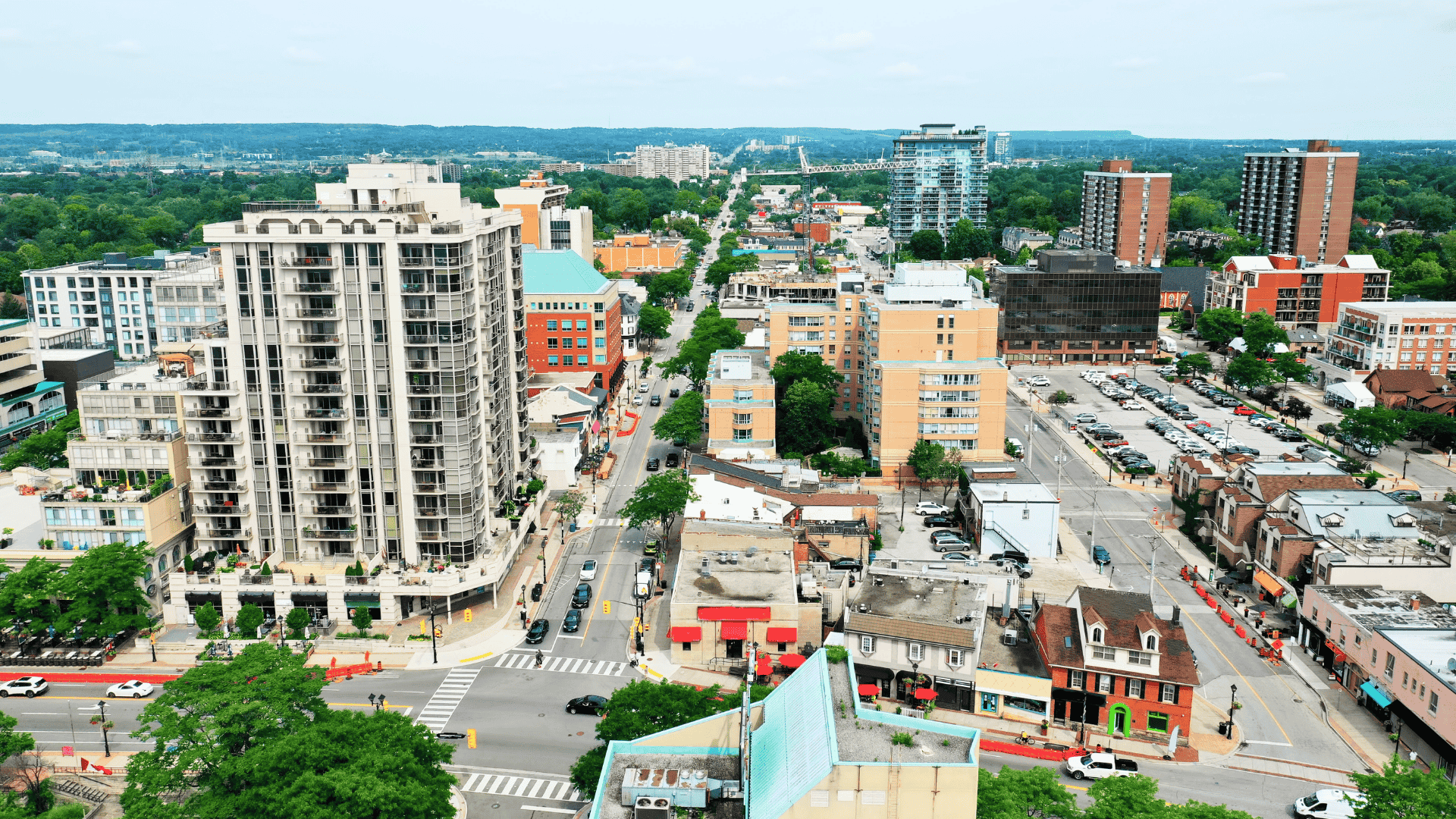 Aerial view of a cityscape with mid-rise buildings, streets, cars, and trees on a clear day.