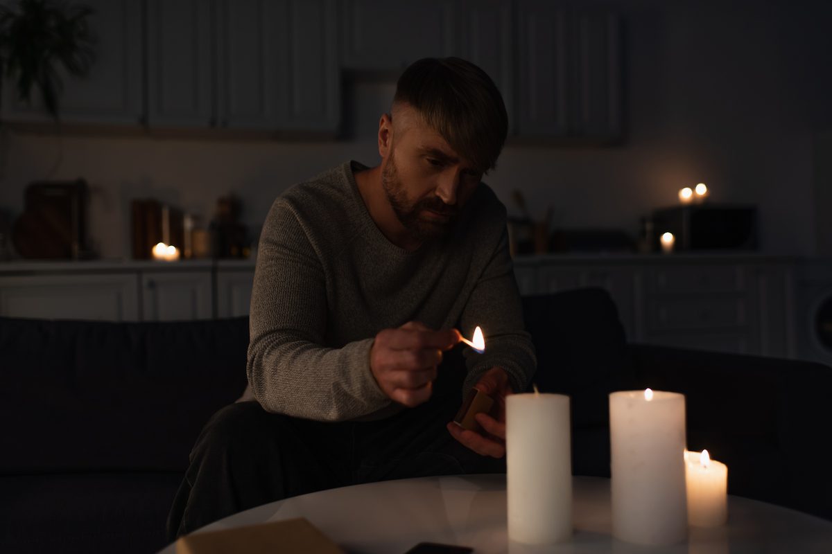 A man lights a match to ignite a candle on a table in a dimly lit room with other candles.