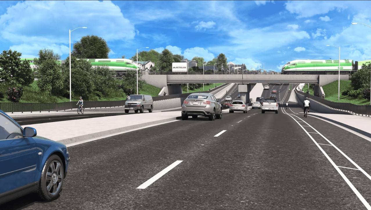 A multi-lane road with cars, cyclists, and pedestrians passes under a bridge with trains and a station visible above.