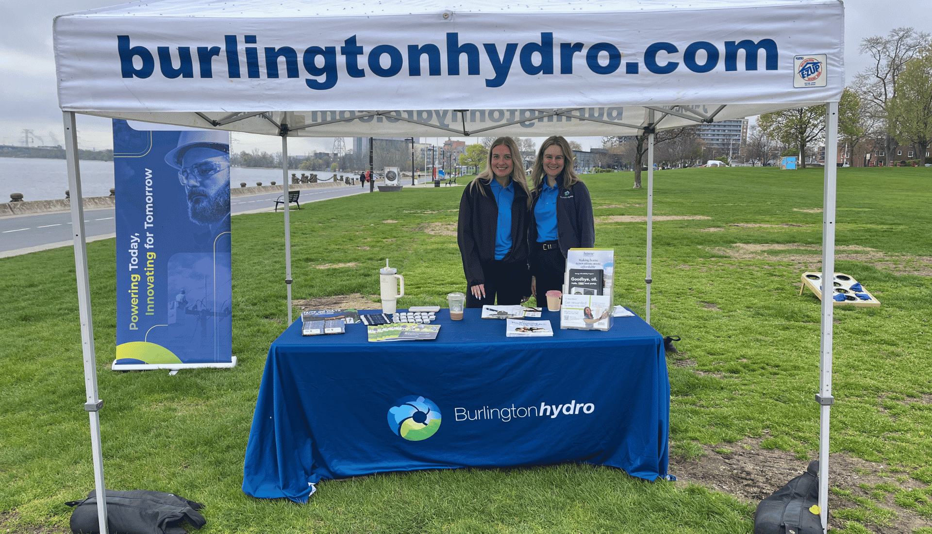 Two people stand behind a Burlington Hydro stall with informational materials under a branded canopy at an outdoor event.