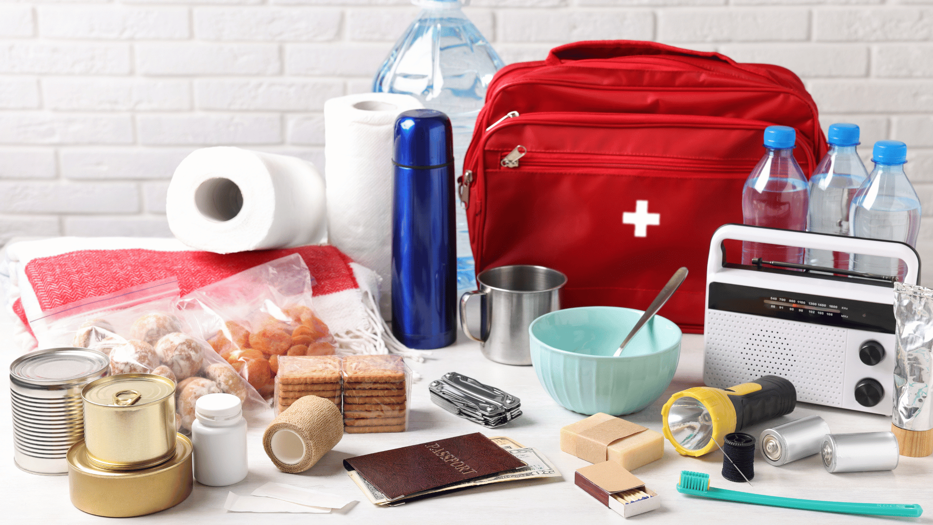 Emergency kit with food, water, first aid bag, radio, torch, toiletries, and other survival supplies on a table.